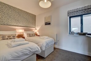 A modern bedroom with two beds, a large window with a view, and a textured wall above the beds. - 3 Bed in Woolacombe (oc-5byron) (Woolacombe)