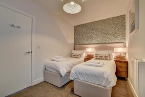 Quarto com duas camas, uma porta branca, parede texturizada e luminária pendente.