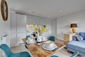 A modern kitchen with white cabinets, a wooden dining table set with white plates and bowls, and a vase of yellow flowers.
