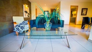 Un salon moderne avec une table basse en verre, un canapé bleu et un plaid à motifs.