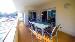 Un balcon avec une table et des chaises en verre, une plante en pot et une vue sur la ville.