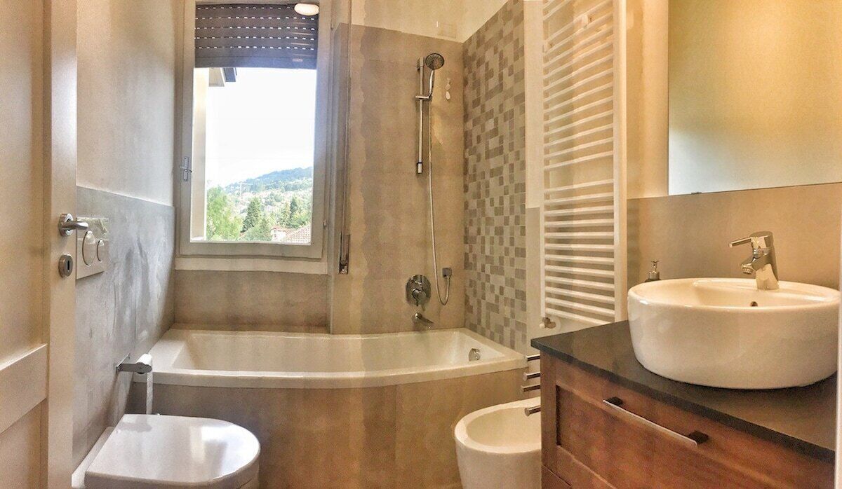 A bathroom with a bathtub, a toilet, a sink, and a window with a view of greenery.