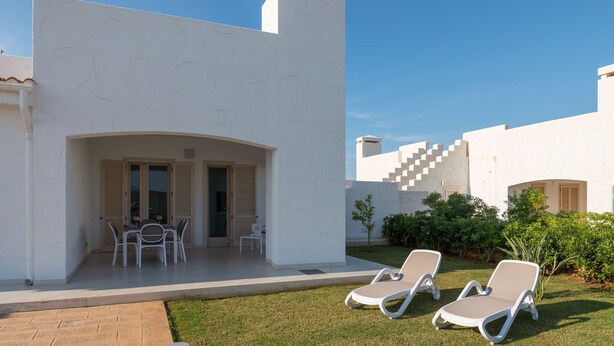 Un espace extérieur moderne comprenant une terrasse, deux fauteuils de jardin, une table avec des chaises et un petit jardin.