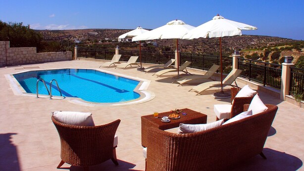 A pool area with lounge chairs and umbrellas, overlooking a scenic landscape. - Luxurious Private Villa with Private Pool and Sea Views- 6 min drive from beach (gouves)
