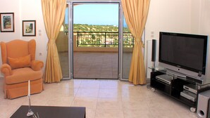 A living room with a sofa, a TV, a small table with a candle, and a balcony with curtains. - Luxurious Private Villa with Private Pool and Sea Views- 6 min drive from beach (gouves)