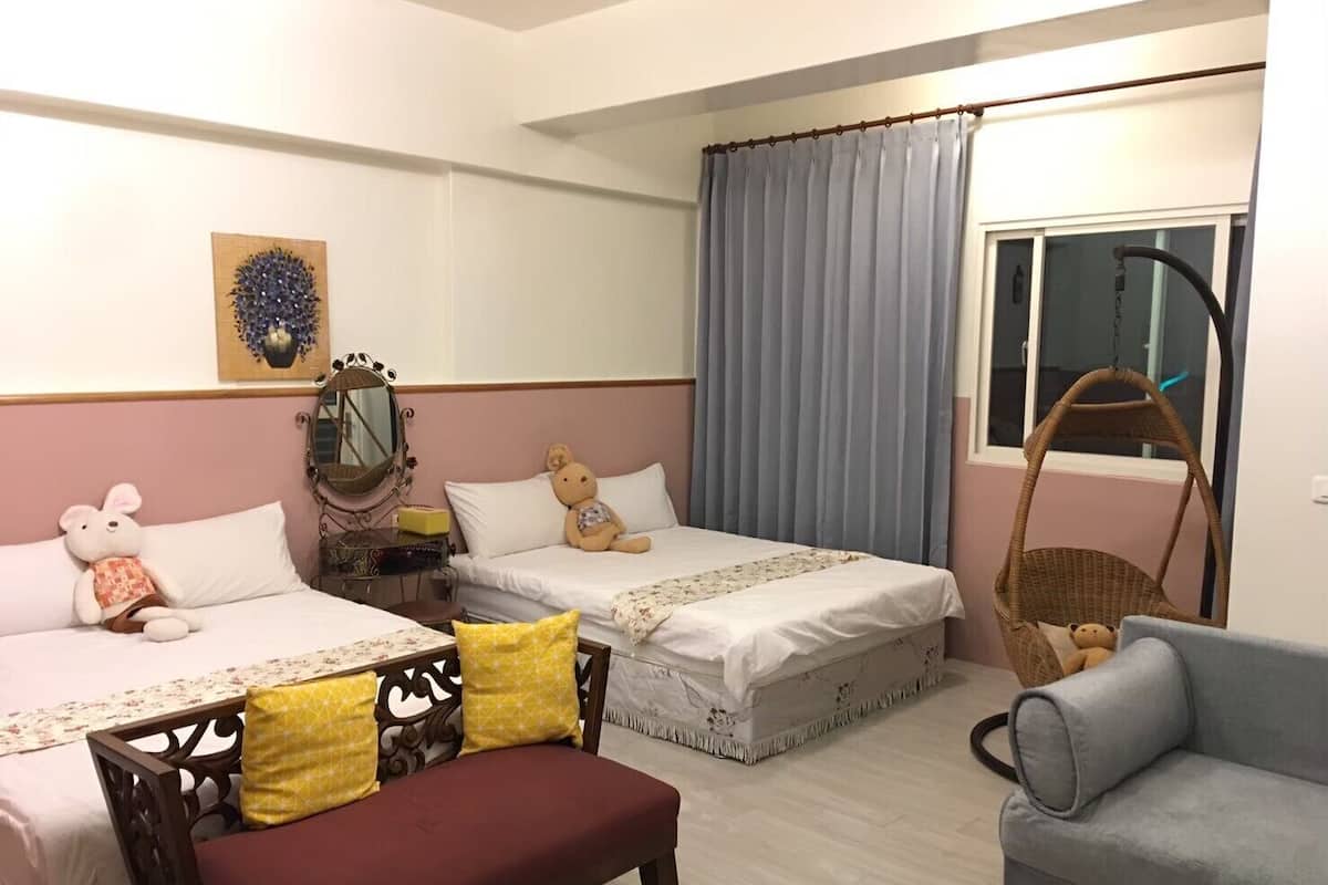 Un dormitorio con dos camas, un banco, una silla, un sillón colgante y una ventana con cortinas.