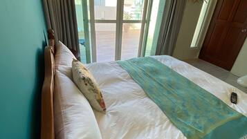 A hotel room with a large bed, a wooden headboard, a view through a sliding glass door to an outdoor area, and a ceiling-mounted air conditioning unit.