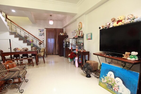 A living room with a staircase, a dining table, a sofa, a TV, and a painting. - Beauty Home Homestay (Hualien City)