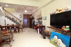 A living room with a staircase, a dining table, a sofa, a TV, and a painting.