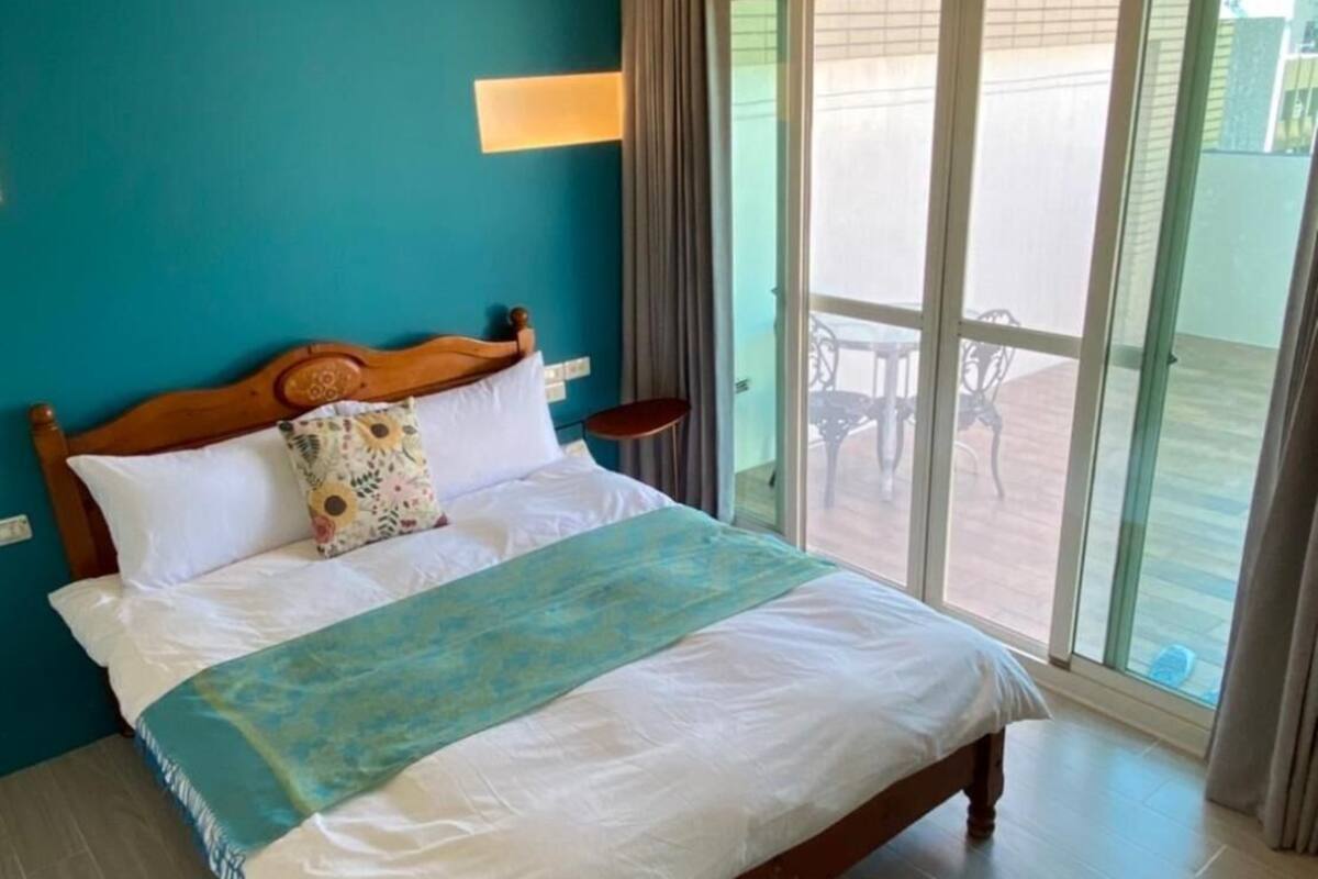 Una habitación de hotel con una cama grande, vistas del patio exterior y una pared color turquesa.