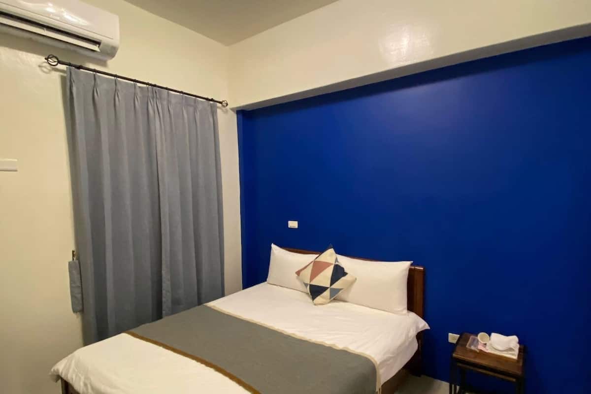 Un dormitorio con cama, mesita de noche, pared de acento azul y equipo de aire acondicionado.