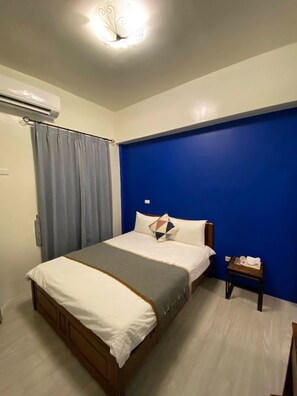 A bedroom with a bed, a nightstand, a blue accent wall, and an air conditioning unit. - Beauty Home Homestay (Hualien City)