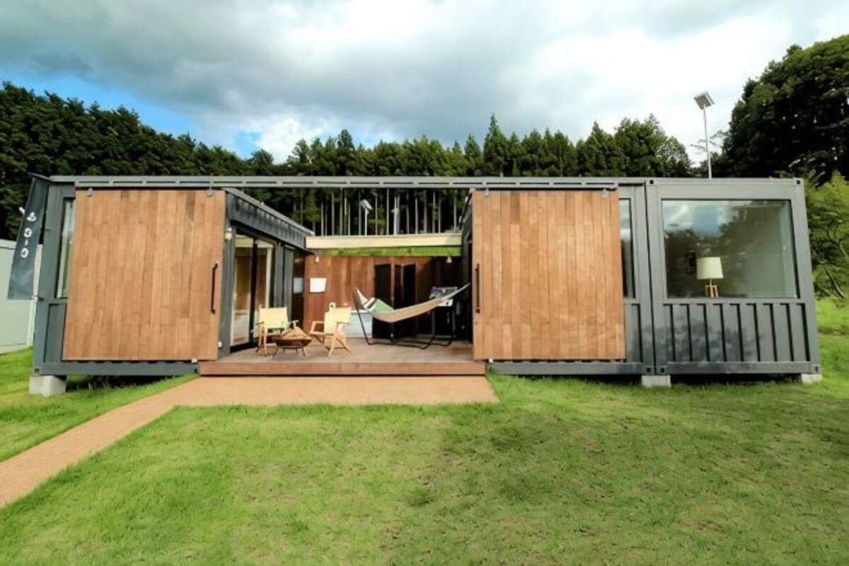 A modern container home with a deck, a hammock, and a small table.