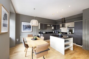 Een moderne keuken met grijze kastjes, een houten eettafel en een hangende lamp.
