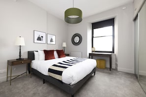 Un dormitorio moderno con una cama, mesitas de noche, un escritorio y una ventana.