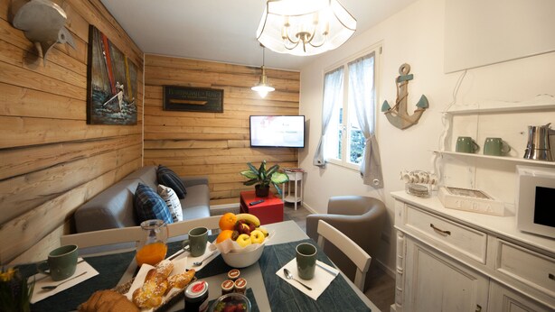 Una sala de estar acogedora con un muro de madera, un sofá cómodo, una mesa de comedor con alimentos para el desayuno y un televisor en la pared.