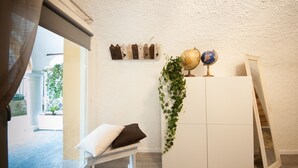 Una habitación con un armario blanco, un banco con cojines, una planta colgante y un estante de pared con adornos.