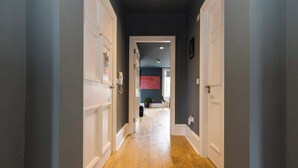 Un couloir doté d’un plancher en bois, de portes blanches et d’un mur de couleur sombre.