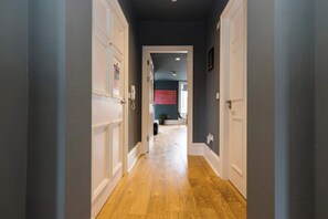 Un pasillo con suelo de madera, puertas blancas y una pared oscura.