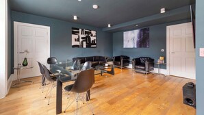 Un salon moderne avec une table à manger en verre, des canapés en cuir noir et un grand écran mural.