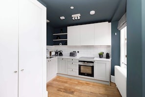 A kitchen with white cabinets, a black oven, and a wooden floor.
