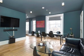 A modern living room with a glass coffee table, leather sofa, and a flat-screen TV mounted on the wall.