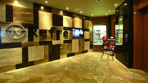 A modern hotel lobby with a stone-patterned floor, a large 'Reflex' sign, and a digital screen displaying content. - Nikoh Capsule Hotel Refre - Hostel - Caters to Men (Sapporo)