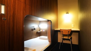 A compact hotel room with a single bed, a small desk with a chair, and a wall-mounted light. - Nikoh Capsule Hotel Refre - Hostel - Caters to Men (Sapporo)