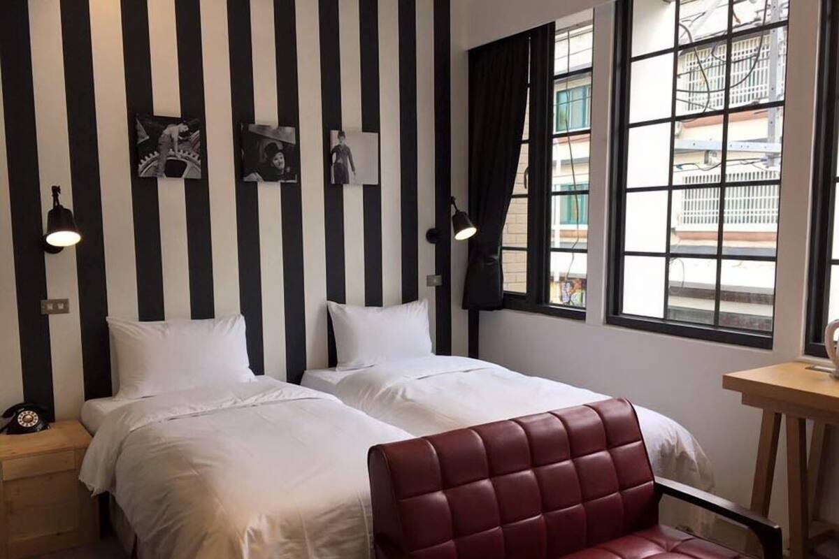Una habitación de hotel con dos camas, un sillón de cuero rojo y paredes a rayas negras y blancas.