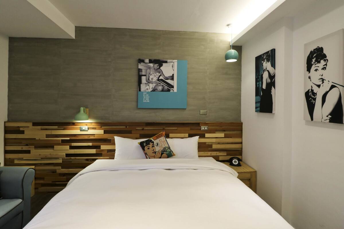 Un dormitorio moderno con cabecera de madera, cama con ropa de cama blanca, mesita de noche con lámpara y decoración en la pared.