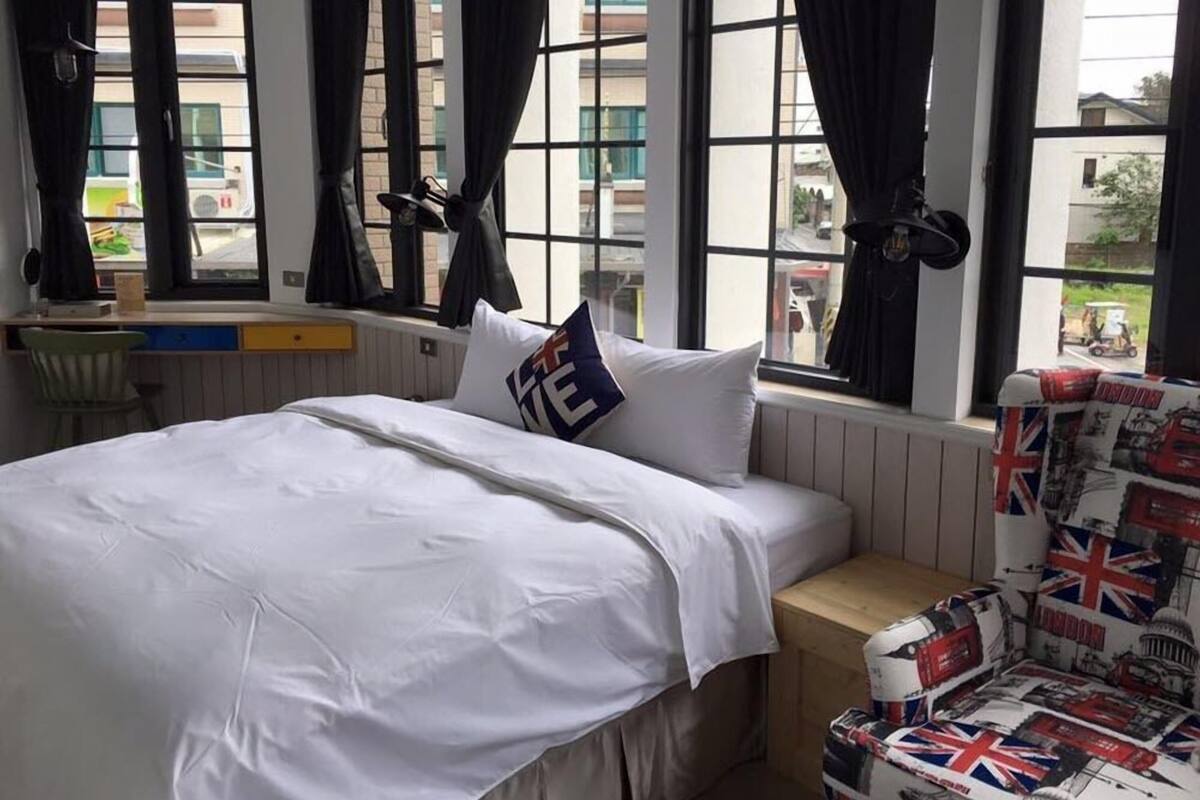 Habitación de hotel con cama, escritorio y silla. Ventanas con cortinas y vista al exterior.