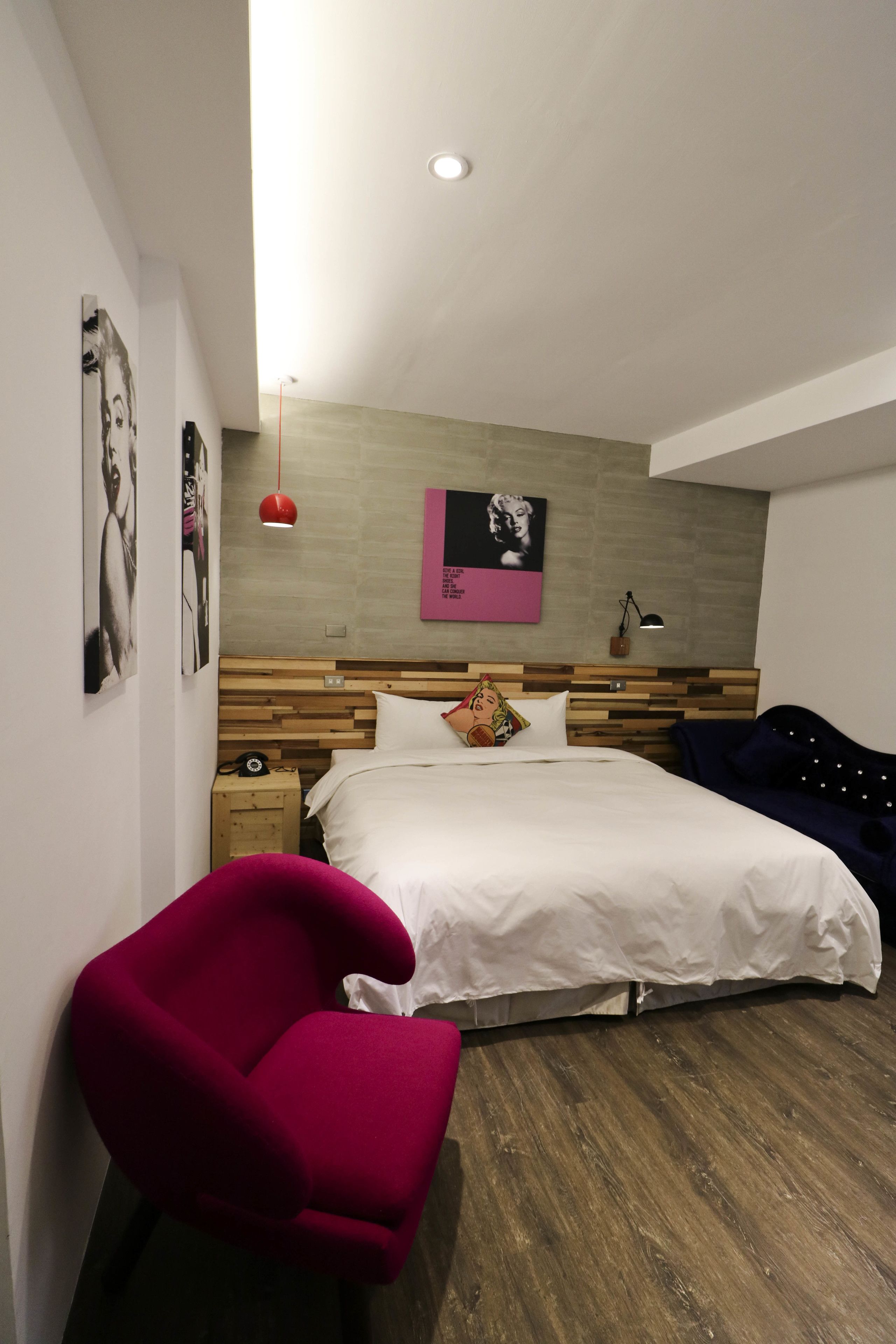 Ein modernes Schlafzimmer mit einem Holzkopfteil, einem weißen Bett, einem roten Sessel und Holzboden.