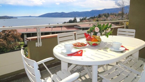 A round white table with chairs on a balcony overlooking a lake and mountains. - Selva 1 lake view apartment in Ghiffa with pool (Ghiffa)
