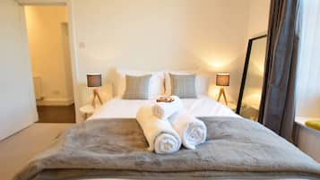 A hotel room with a bed, two bedside lamps, a large window with curtains, and a door leading to another room.