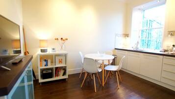 A modern kitchen with white cabinets, a round dining table with white chairs, a built-in oven, and a window with a view of a building.