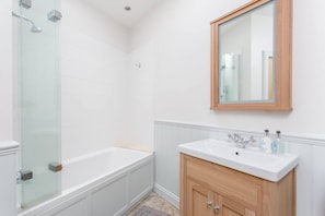 A bathroom with a glass-enclosed shower, a white bathtub, a wooden vanity with a sink, and a mirror above the vanity.