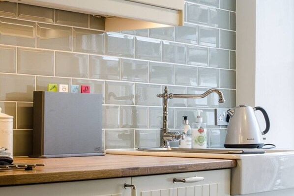 Una cocina con salpicadero de azulejos, un hervidor de acero inoxidable y una encimera de madera.