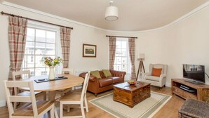 A living room with a dining table, sofa, television, and a lamp. - Trendy & Stylish Apartment in Edinburgh's New Town (Edinburgh)