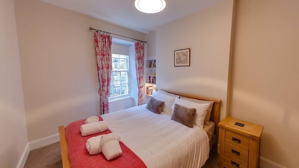 A bedroom with a bed, a nightstand, a window with curtains, and a bookshelf. - Trendy & Stylish Apartment in Edinburgh's New Town (Edinburgh)
