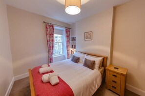 A bedroom with a bed, a nightstand, a window with curtains, and a bookshelf.