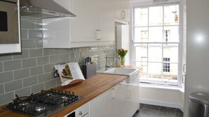 A kitchen with white cabinets, a gas stove, a window with a view of buildings, and a sink. - Trendy & Stylish Apartment in Edinburgh's New Town (Edinburgh)