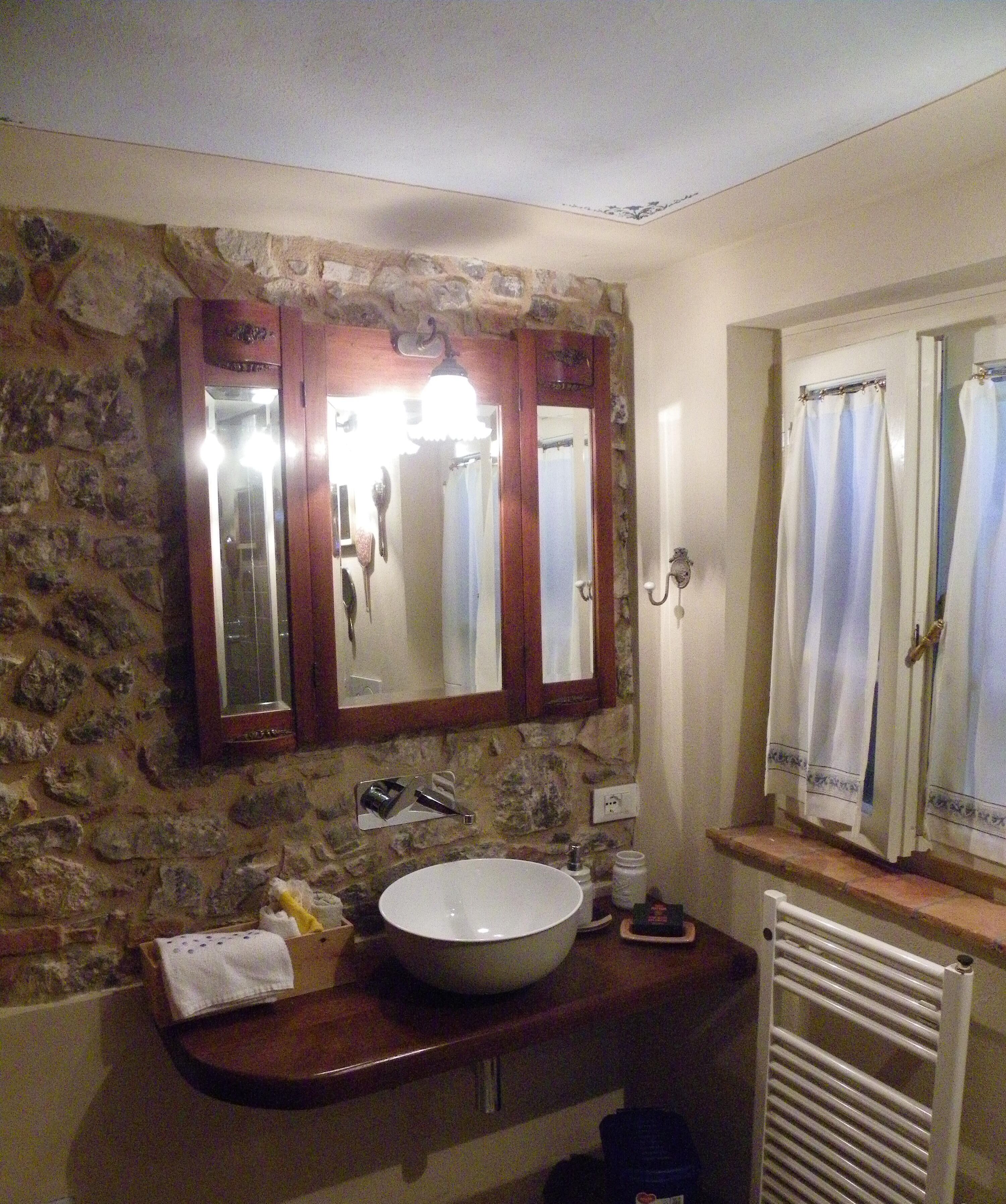 A bathroom with a stone wall, a white sink, a mirror, and a shower curtain.