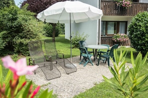 A patio with outdoor furniture, a white umbrella, and a view of a building with a balcony.