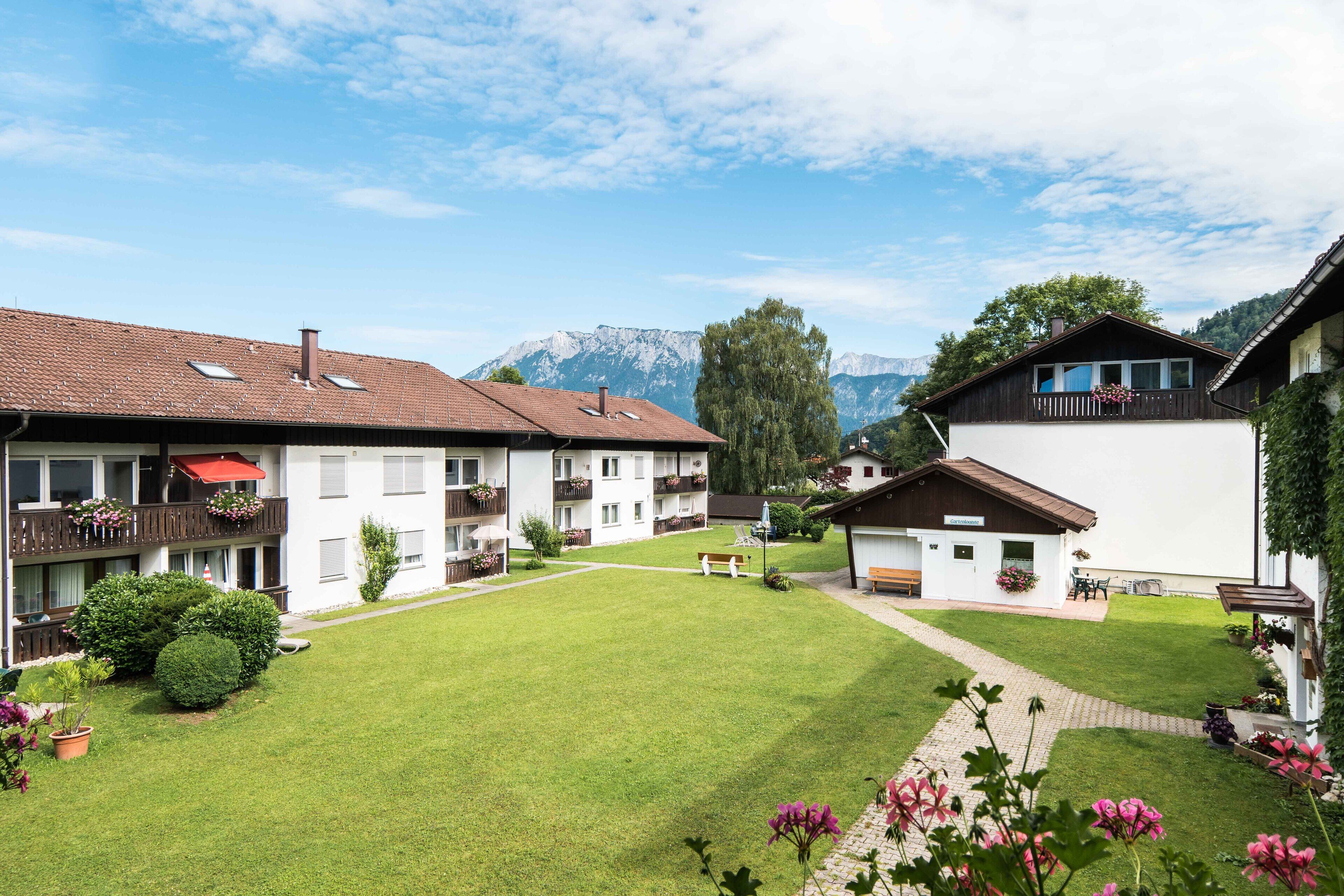 Ein Innenhof mit Rasenfläche, Bänken und einem kleinen Gebäude mit Balkon.