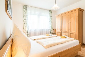 A bedroom with two beds, a wooden wardrobe, a window with curtains, and a hanging light fixture. - E4 Classic apartment***, 53sqm, balcony, suitable for allergy sufferers (Oberaudorf)