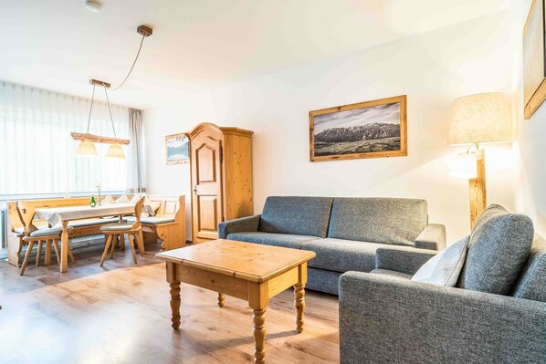 A living room with a wooden coffee table, grey sofa, wooden cabinet, and a dining area with a bench and table. - E4 Classic apartment***, 53sqm, balcony, suitable for allergy sufferers (Oberaudorf)