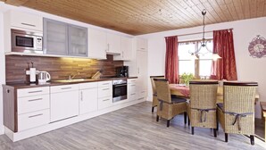 Una cocina moderna con armarios blancos, microondas y cafetera. Hay una zona de comedor con sillas de mimbre y una mesa.