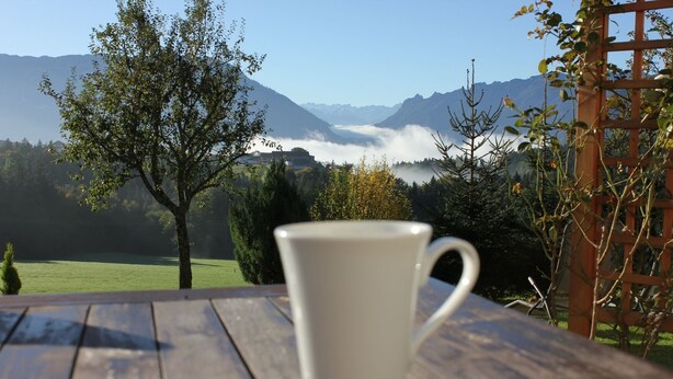 A white mug on a wooden table with a mountain view in the background. - Ferienwohnung im Erdgeschoss 45 qm, Schlafzimmer, Wohn-/Schlafraum, separate Küche, 4 Sterne, max. 4 Personen (Anger)