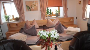 A cozy bedroom with a bed, pillows, a bedside table with a bottle and glass, and a window with curtains. - Ferienwohnung im Erdgeschoss 45 qm, Schlafzimmer, Wohn-/Schlafraum, separate Küche, 4 Sterne, max. 4 Personen (Anger)
