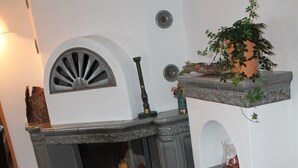 A corner fireplace with a mantelpiece, a small shelf with decorative items, and a wicker basket with logs. - Ferienwohnung im Erdgeschoss 45 qm, Schlafzimmer, Wohn-/Schlafraum, separate Küche, 4 Sterne, max. 4 Personen (Anger)